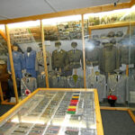 Ausstellung zur Bundeswehr mit Soldatenuniformen, Ausrüstung und militärischem Arbeitsbereich in einer Museumsvitrine